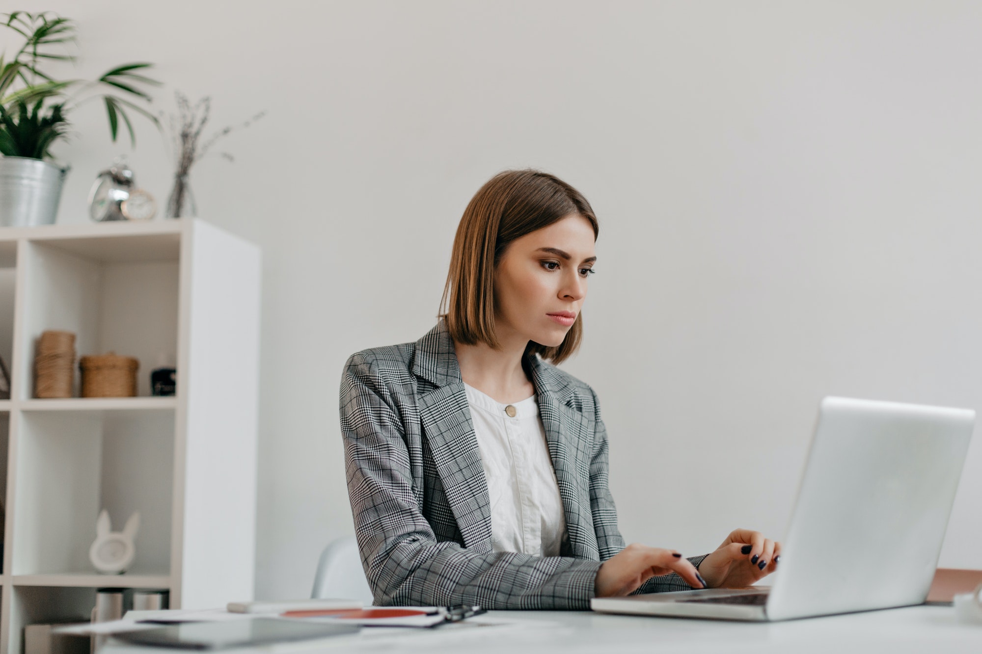 Attractive blonde woman typing letter in MacBook at her workplace. Photo of lady in stylish jacket